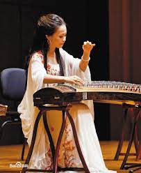 A musician in Chinese dress, playing a traditional Chinese instrument called a Guzheng