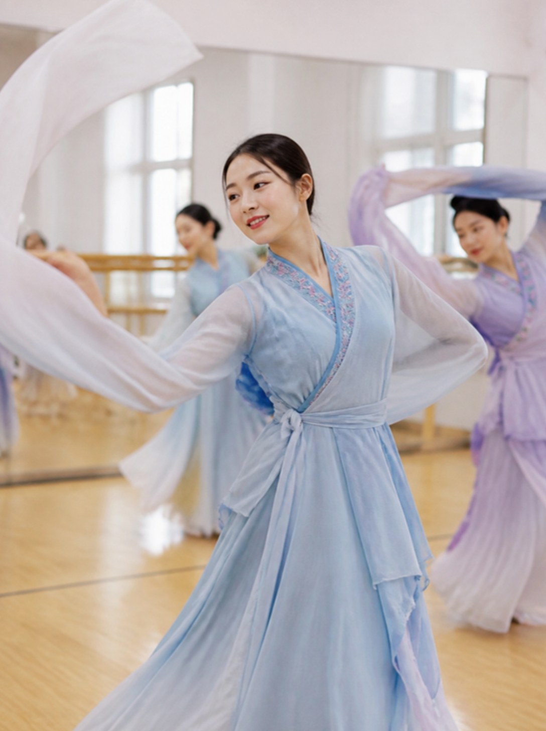 A dancer in a pale blue Chinese classical dance costume swirls her long water sleeves in a studio