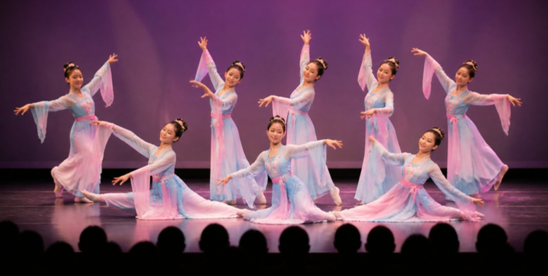 Dance students in flowing blue and pink costumes perform on stage at a showcase